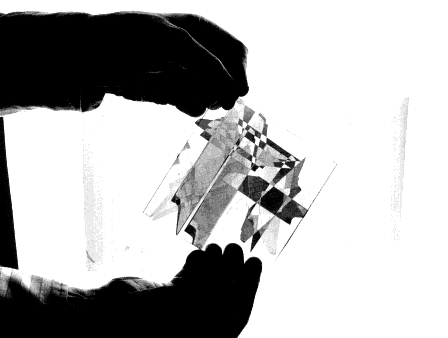 Händer som håller ett ark OH-plast som försetts med tejpbitar. Foto.