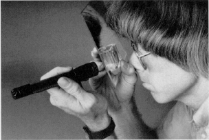 Pojke granskar sin pupill genom förstoringsglas och spegel. Foto.