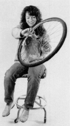 Kvinna som håller ett cykelhjul sittande på en kontorsstol. Foto.