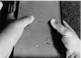 Tummar som pressar mot skivor av plexiglas och framkallar mönster. Foto.