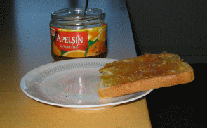 Rostad macka balanserar på assiett med marmeladburk i bakgrunden. Foto.