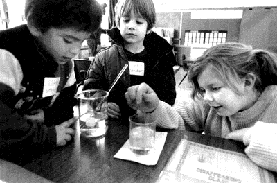 Barn om studerar en glasstav som är nerdoppad i olja i en glasbägare. Foto.