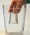 Hand som håller snapsglas med luft i under vatten i en vattenfylld bägare. Foto.