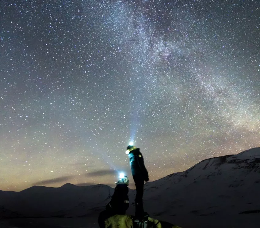Två personer som lyser med ficklampor upp mot stjärnhimlen. Foto.